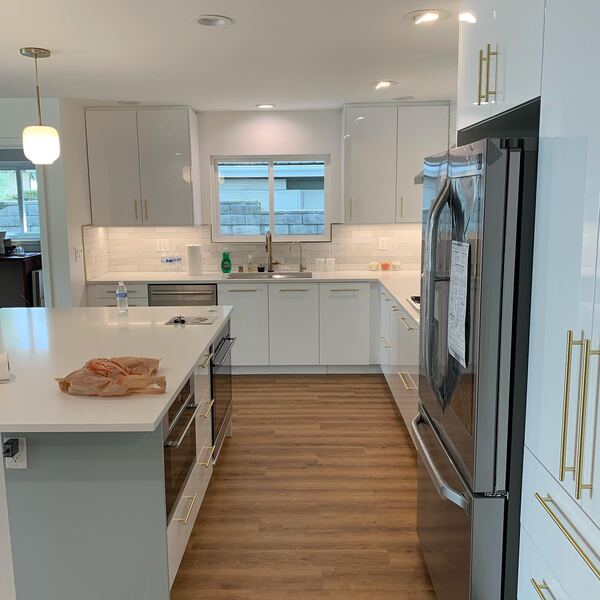 White kitchen cabinets with brass pulls and a stainless refrigerator